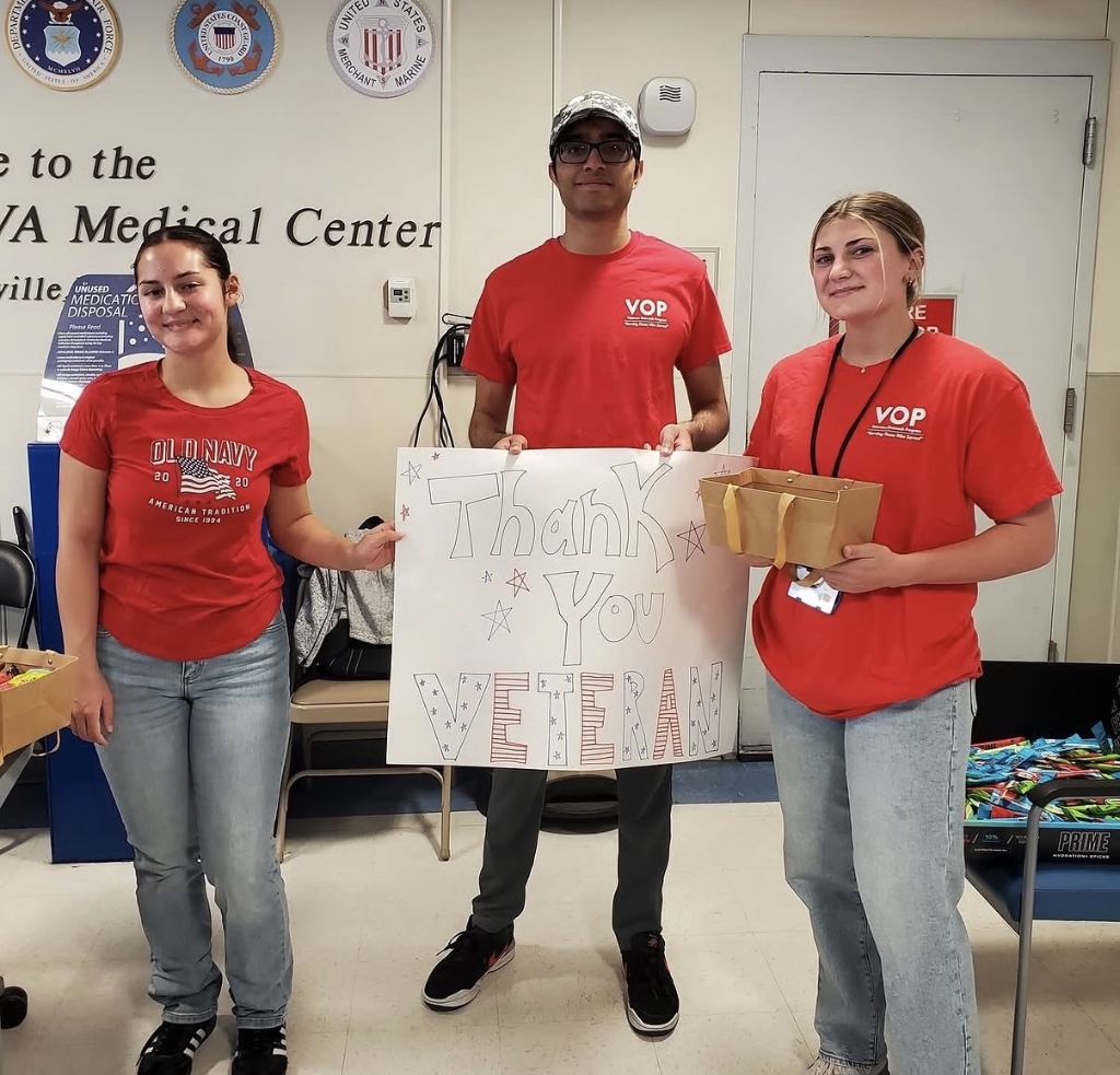 VOP student volunteers in red VOP shirts holding Thank You Veteran sign at the VA Medical Center